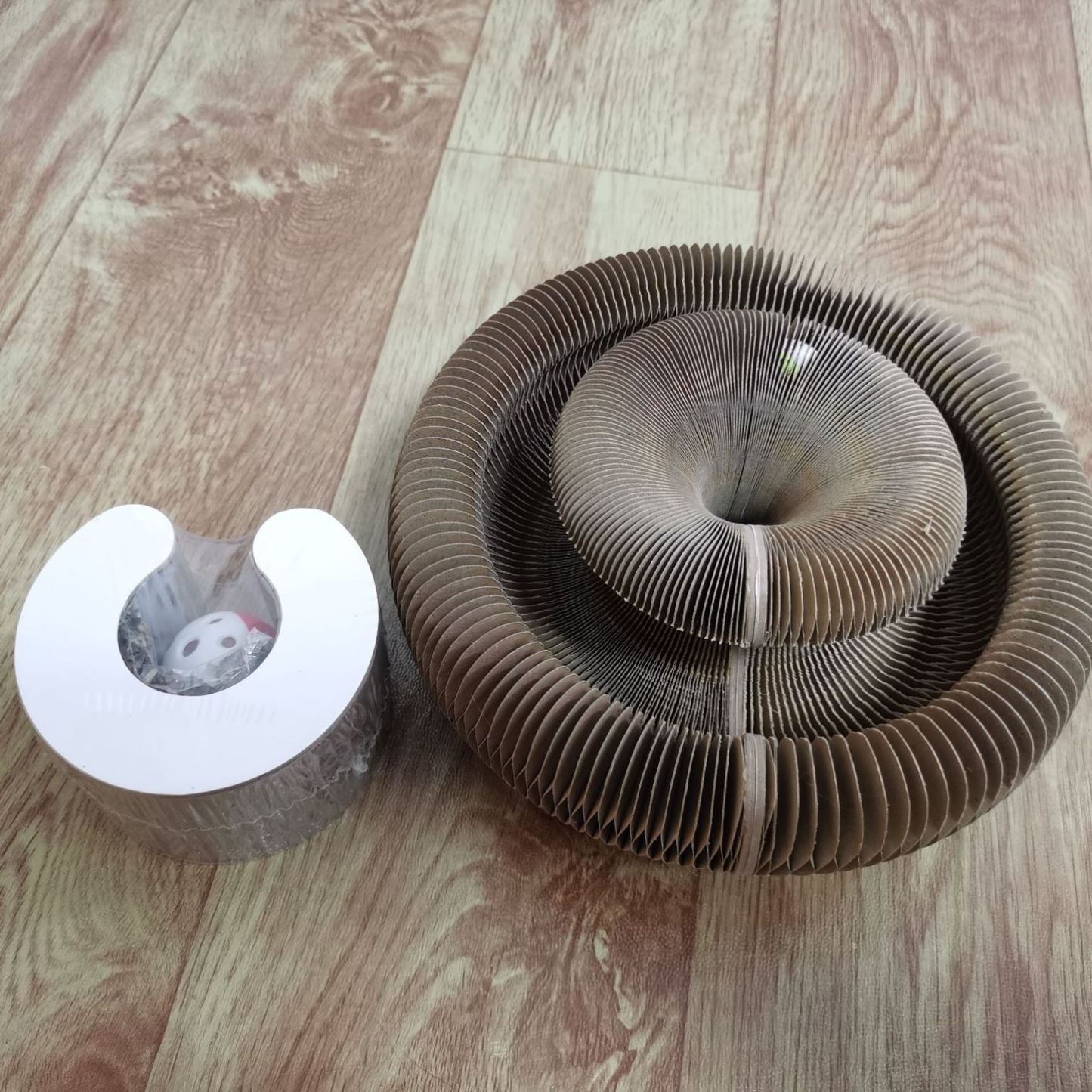 Pounce and Play Cat Scratcher made of corrugated paper with a compact spiral design and included ball toy on wood floor.